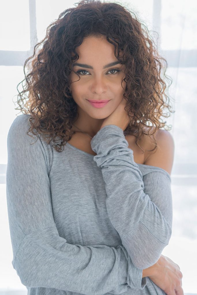 Natural light boudoir image of curly haired mixed race woman